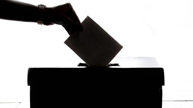 A black and white stock image of a person depositing their ballot in a ballot box.
