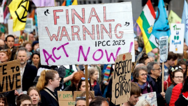 A photo of a protest rally, with a large sign reading 'Final Warning, Act Now' in the centre of the image.