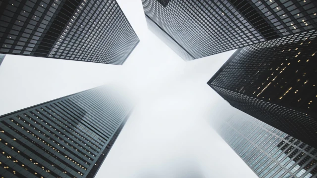 An AI generated stock photo of five tall office buildings, seen from the ground. All office buildings are generic offices, with lots of cladding and glass. The top of some of the high-rises disappears in the clouds.