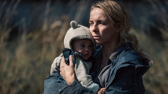 A scene from The End We Start From, in which a woman (played by Jodie Comer) holds a child while looking into the distance.