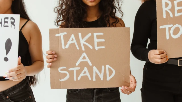 A stock photo of a women holding up a cardboard sign with the text Take A Stand.