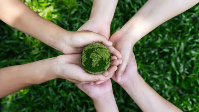 A stock photo of five people carefully holding a small bit of earth.