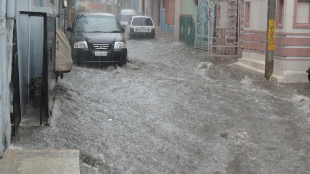 A photo of a flooded street in a city. Where there was a street there is now a stream of water.