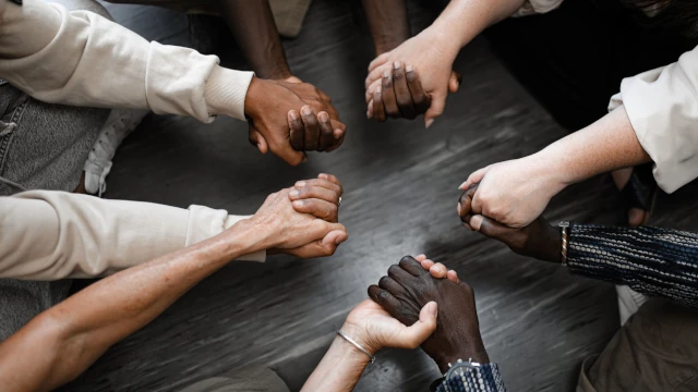 A close-up image of five people in a circle holding hands.