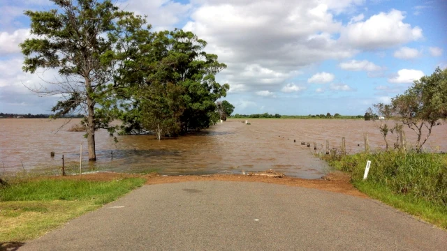 A photo of a road which goes into what looks like a large lake. You can still see trees lining what previously was the road.