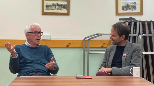 A photo of Rupert interviewing Paddy Flynn. They are sitting at a table and Paddy is looking in the distance while talking and gesticulating.