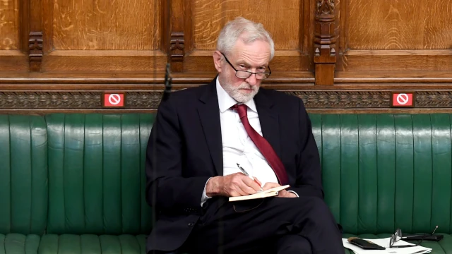A photo of Jeremy Corbyn, sitting alone on one the green benches in the House of Commons.
