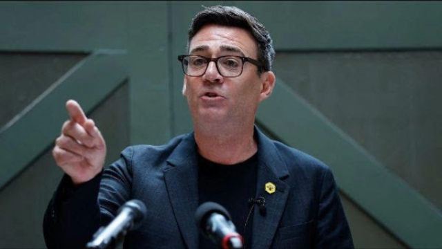 Photograph of Andy Burnham, pointing, behind a microphone stand